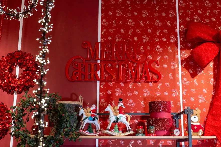 Parete rossa con la scritta Merry Christmas, ghirlande, cavallini a dondolo e scatole decorate