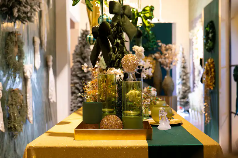 Un corridoio dello showroom allestito per Natale: tavolo con tovaglia verde e oro, ghirlande alle pareti, alberi innevati sul fondo