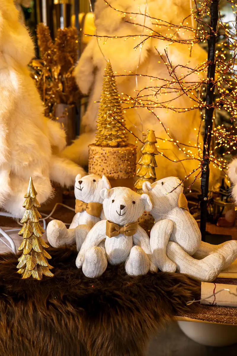 Orsi bianchi di peluche con sciarpe dorate accanto ad alberelli dorati