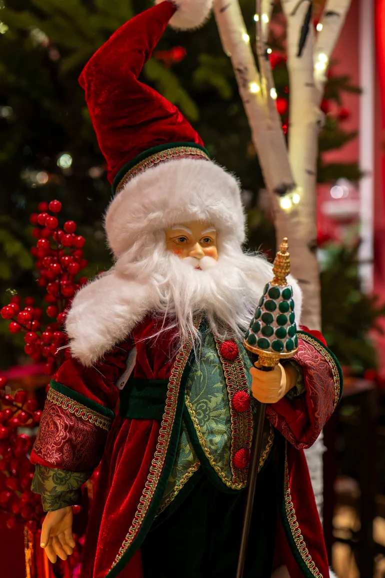 Babbo Natale in velluto rosso e verde con barba bianca davanti all'albero